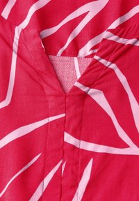 Vaaleanpunainen kangas valkoisilla abstrakteilla viivoilla, jossa on V-pääntie ja näkyvät ompeluyksityiskohdat. Tekstuurin pinnan vaikutelma on sileä ja kevyt.