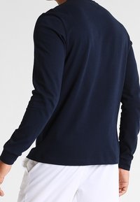 Camisa de manga larga azul marino hecha de tela suave, con escote redondo y diseño ajustado sin logos ni estampados visibles.