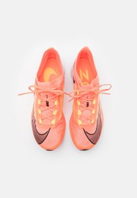 Chaussures de sport orange avec une surface texturée, des accents noirs et des lacets jaune fluo. Présente un logo Nike bien en vue sur le côté.