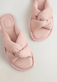 Minkšti rožiniai languoti pūkšti šlepetės su plačiomis susikertančiomis juostelėmis ant šviesaus fono, skirtos patalpų komfortui.