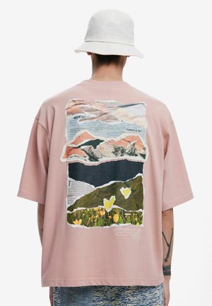 Roze T-shirt met korte mouwen, met een collageprint op de achterkant, die bergen en bloemen toont met gescheurde papier randen; ontspannen pasvorm.