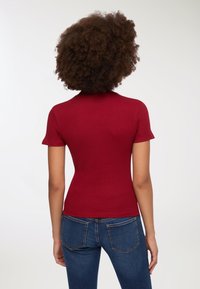 Maglietta rossa a righe con maniche corte, collo alto, silhouette aderente e superficie liscia. Abbinata a jeans in denim blu.