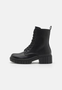 Botas negras hasta el tobillo hechas de cuero sintético. Tienen una punta redondeada, cordones en la parte delantera, un tacón grueso y una lengüeta en la parte trasera.