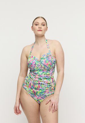 Vrouw die een kleurrijk halternek badpak met een geplooid, abstract patroon draagt, staand tegen een effen lichte achtergrond.