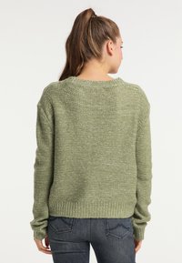Grüner gestrickter Pullover mit strukturierter Oberfläche, runden Halsausschnitt und geripptem Saum und Ärmelbündchen. Kombiniert mit dunklen Jeans, von hinten gezeigt.