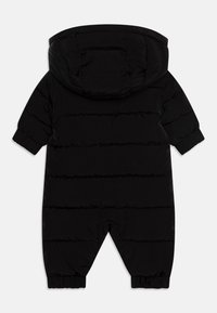Combinaison de neige noire en doudoune avec capuche. Présente des lignes matelassées, des poignets élastiques et des jambes effilées, fabriquée à partir d'un matériau lisse et isolé.