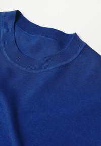 Pull bleu tricoté à col rond, étalé à plat sur une surface blanche, montrant la texture et les détails du col côtelé.
