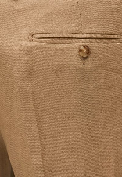 Κοντινό πλάνο σε μπεζ υφασμάτινο παντελόνι με μία πίσω τσέπη με καφέ κουμπί.