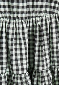 Robe en vichy avec motif à carreaux noirs et menthe, comprenant des volants froncés et un tissu texturé. Matériau structuré et léger.