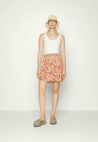 Top branco de alças combinado com uma saia mini floral com flores vermelhas, amarelas e azuis. Usado com sandálias cinzas e um chapéu de balde amarelo.