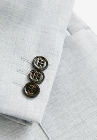 Tessuto grigio chiaro con un motivo testurizzato, caratterizzato da tre bottoni scuri lungo il bordo, che mostrano sottili dettagli di cucitura.