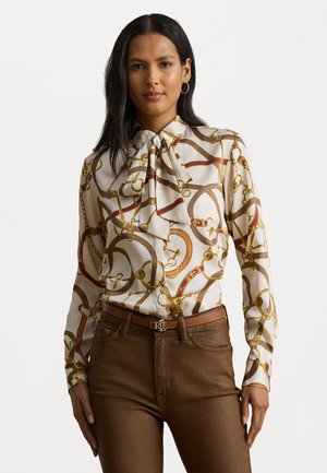 Blusa de manga longa em seda creme com um padrão de corrente em dourado, vermelho e castanho. Apresenta um laço no colarinho e uma silhueta ajustada.