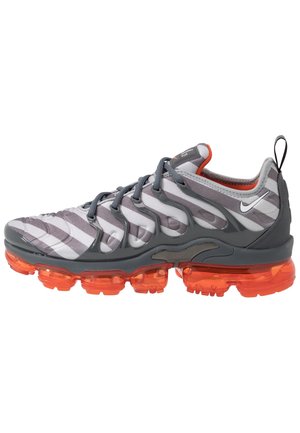 Grijs-witte Nike sneaker met donkergrijze overlays, oranje transparante zool en kleine witte Nike swoosh aan de zijkant.