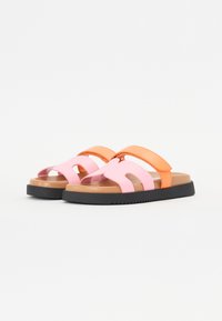 Tvåfärgade halkskyddssandaler med en rosa syntetiska ovandel med utskärningar och ett kontrasterande orange band. Svartrandig gummisul.