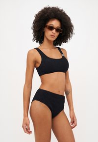 Textúrált anyagból készült fekete, kétrészes bikini szett; a fényes melltartó széles pántokkal és oldalsó díszítéssel rendelkezik. A magas derekú bugyi tökéletesen kiegészíti a megjelenést.