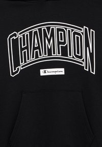 Μαύρο φούτερ με κουκούλα από βαμβάκι, με μεγάλο λευκό λογότυπο «CHAMPION» και μια μικρή ετικέτα στο κάτω μέρος. Διαθέτει μπροστινή τσέπη.