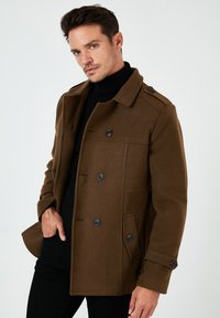 Chaqueta marrón de mezcla de lana con cuello, diseño de doble botonadura y botones negros. Cuenta con dos bolsillos laterales y una textura suave.