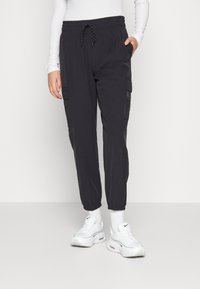 Black cargo pants with a drawstring waist, featuring side pockets, elastic cuffs, and a smooth texture. Paired with white athletic shoes.