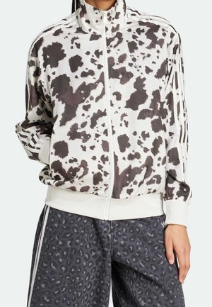 Person wearing a white and black spotted zip-up jacket and dark gray leopard-print pants with white stripes on the sides.