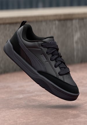Black athletic shoe with smooth leather upper, textured black accents, thick laces, and a cushioned sole, featuring a sleek, modern design.