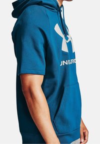 Modrá mikina z bavlny, s klokankou, krátkými rukávy a velkým bílým logem na přední straně. Měkký materiál, jednoduchý design pro přes head.