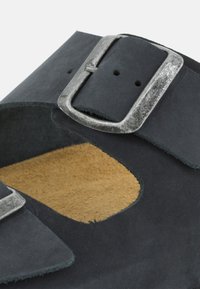 Sandal in camoscio nero con design a taglio, fibbia in metallo argentato e soletta in camoscio beige. Parte superiore testurizzata con accenti a contrasto sulle cinghie.