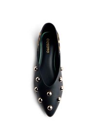 Chaussure noire en cuir à bout pointu avec des clous métalliques dorés sur le dessus. Présente une doublure verte contrastante et une texture lisse.