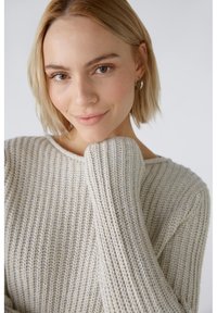 Hellbeige gestrickter Pullover mit ribbeliger Textur, breitem Halsausschnitt und leicht übergroßen Ärmeln.