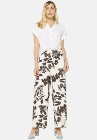 Camicia bianca a maniche corte con bottoni, abbinata a pantaloni larghi con un motivo floreale marrone su sfondo crema, completata da décolleté azzurro chiaro.