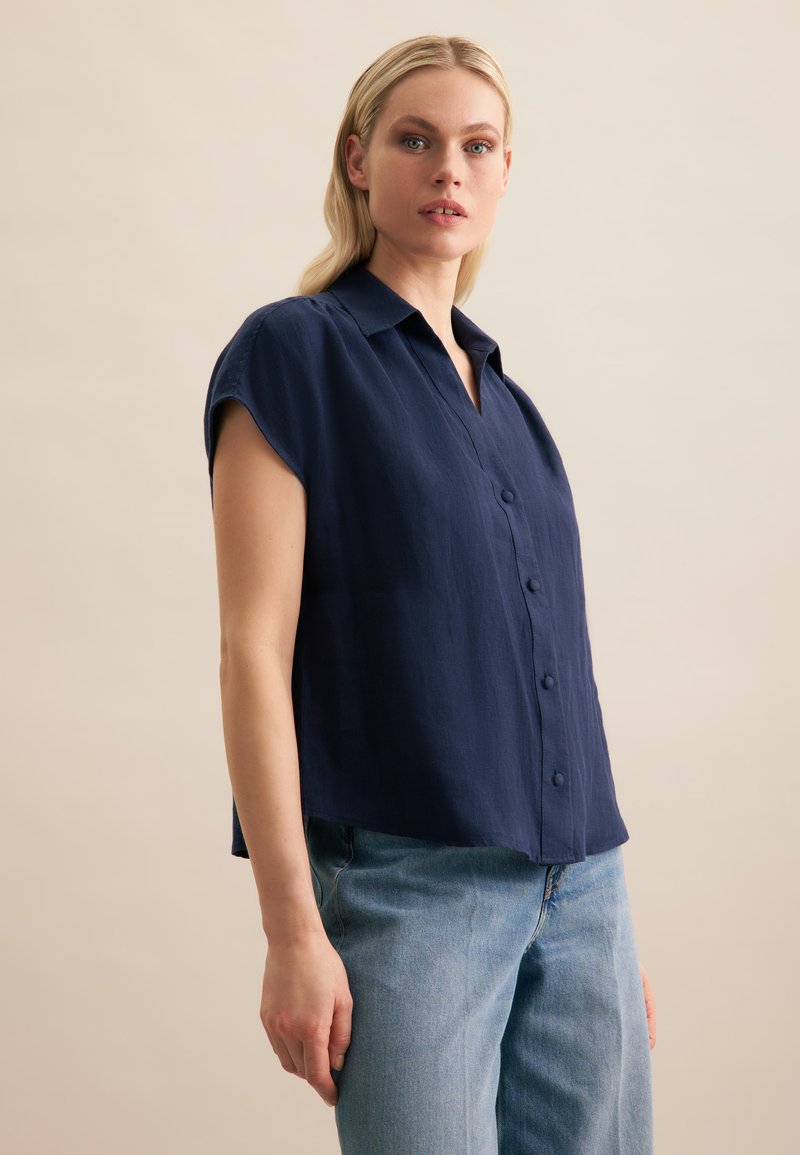 Chemise à manches courtes bleu marine avec un col et une coupe droite, fabriquée à partir d'un tissu léger et texturé.