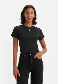 Musta lyhythihainen croppitoppi sileästä puuvillakankaasta, jossa on pyöreä pääntie, yhdistetty korkeavyötäröisiin mustiin farkkuihin.