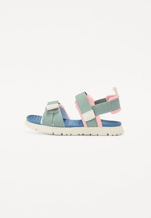 Sandal with light green fabric straps, pink accents, and a blue insole. Features a textured white rubber outsole and adjustable closures.