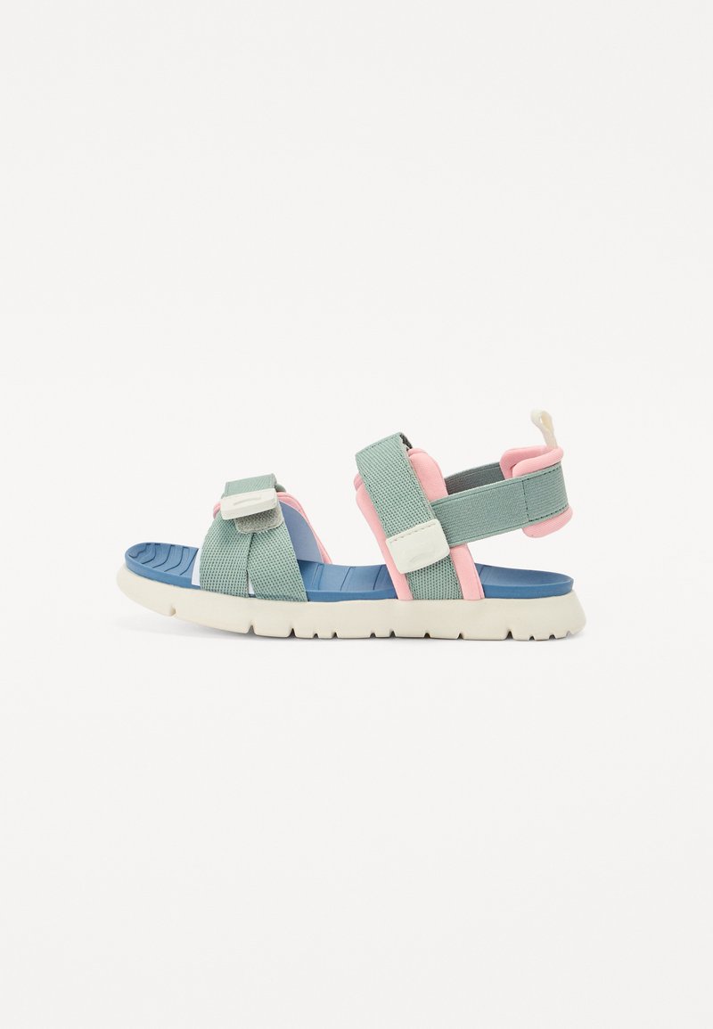 Sandal com tiras de tecido verde claro, detalhes em rosa e uma palmilha azul. Apresenta uma sola exterior de borracha branca texturizada e fechos ajustáveis.