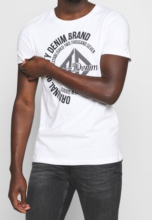 Valkoinen lyhythihainen t-paita, jossa on musta pyöreä graafinen teksti, pyöreä kaula-aukko ja rento istuvuus. Yhdistetty tummanharmaisiin farkkuihin.