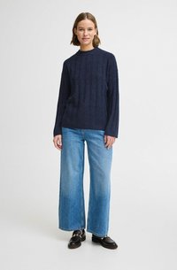 Maglione a coste di colore blu navy con colletto alto, abbinato a jeans a gamba larga di colore azzurro e mocassini neri. Tessuto morbido, vestibilità casual.