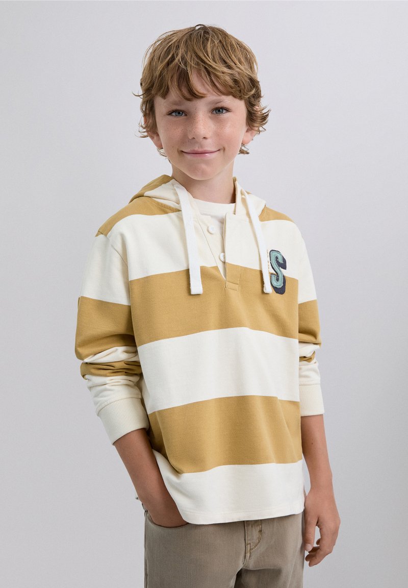 Sudadera a rayas amarilla y blanca con un bolsillo frontal y capucha con cordón. Presenta un tapeta con botones y la letra "S" bordada.