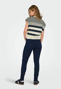 Maglione a righe a maniche corte in crema e blu navy, abbinato a jeans skinny blu navy e sneakers blu navy con dettagli bianchi.