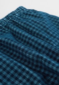 Tissu à carreaux bleus avec un tissage texturé. Le motif présente des carreaux bleus foncés et clairs, avec une taille élastiquée visible en haut.