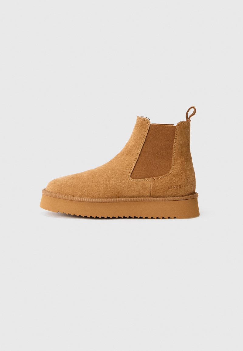 Braune Wildleder-Stiefelette mit elastischen seitlichen Einsätzen, einem Zuglasche an der Rückseite und einer geriffelten Gummisohle, präsentiert auf einem weißen Hintergrund.