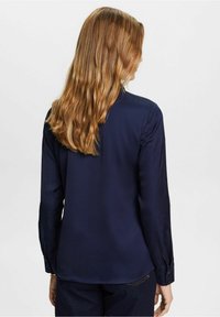 Mörkblå långärmad skjorta med en slät textur, subtil lyster och knäppte ärmslut. Har rundad nederkant och ryggsömdesign.