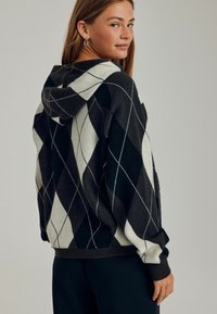 Hoodie w czarno-białym wzorze w romby, wykonany z miękkiego materiału, o luźnym kroju i ściągaczowych mankietach, zaprojektowany z myślą o komforcie.