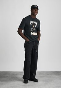 Μαύρο γραφικό μπλουζάκι με σχέδιο αρκούδας, συνδυασμένο με φθαρμένα μαύρα τζιν με στρας. Μαύρα αθλητικά παπούτσια ολοκληρώνουν το σύνολο.