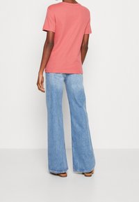 Rosa bomullströja med korta ärmar, i kombination med ljusblå vida jeans, visad bakifrån mot en neutral bakgrund.