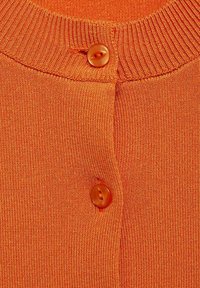 Orange-randig stickad tyg med rund orange knappdetalj i mitten, som har en mjuk textur och en nära vy av halslinningen.