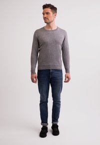 Grau, langärmliger Pullover aus weichem Stoff, kombiniert mit blauen Jeans und schwarzen Sneakers. Der Pullover hat einen Rundhalsausschnitt und eine taillierte Passform.