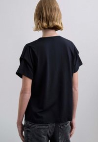 Camiseta negra de manga corta con un ajuste relajado, con un escote redondo y sutiles detalles de hombros abullonados. Fabricada con suave algodón.