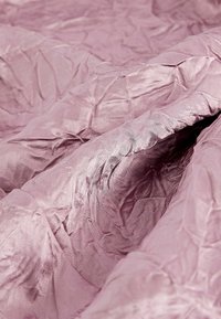 Miękka, pomarszczona tkanina w kolorze mauve z subtelnym połyskiem i widoczną, drobną strukturą splotu, luźno złożona z delikatnymi załamaniami.