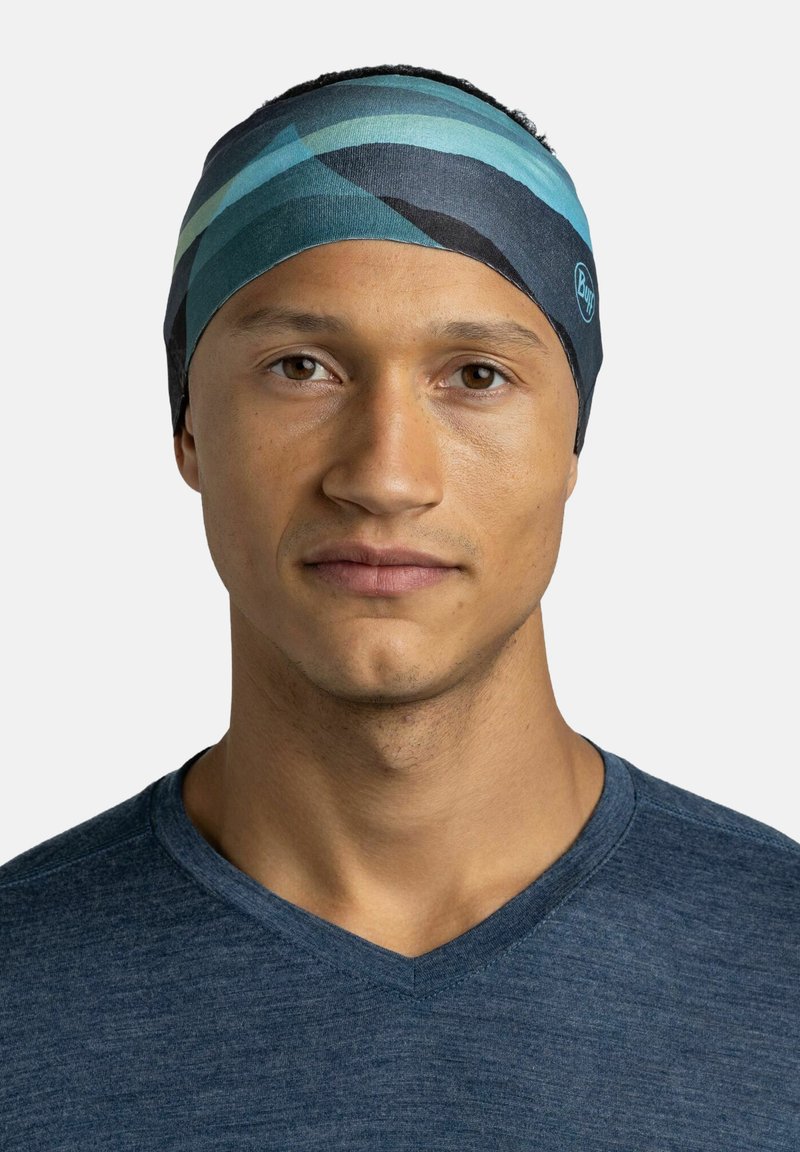 Diadema con rayas azules, verdes y negras; hecha de un tejido suave y elástico; presenta un logotipo en el lateral. Llevada por un modelo con cabello corto.