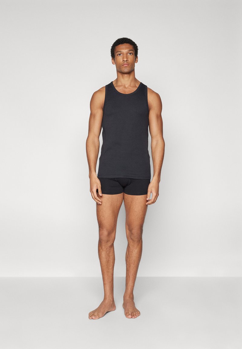 Zwarte tanktop en bijpassende onderbroek van gladde stof, met een eenvoudig ontwerp zonder zichtbare patronen of accenten. Model staat blootsvoets.