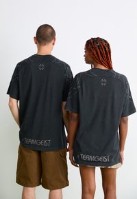 Black cotton T-shirts with short sleeves, featuring a curved design, subtle graphic outlines on the shoulders, and "TEAMGEIST" printed at the hem.